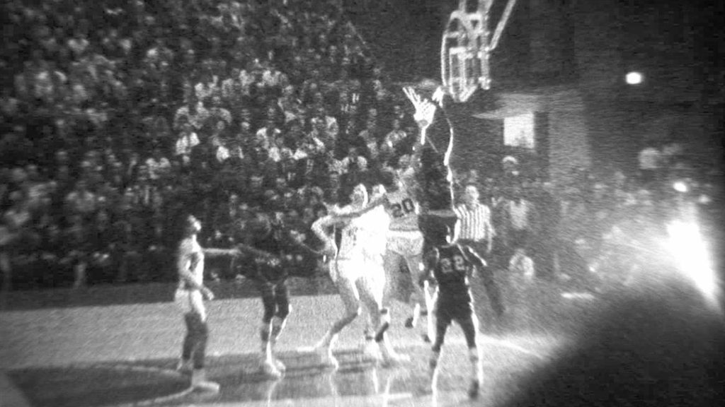 black and white photo of basketball players going for the hoop.